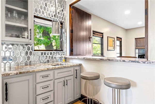 kitchen featuring light stone countertops, tasteful backsplash, kitchen peninsula, and sink