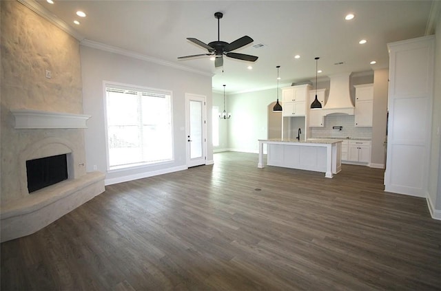 unfurnished living room with ceiling fan, a large fireplace, sink, dark hardwood / wood-style floors, and crown molding