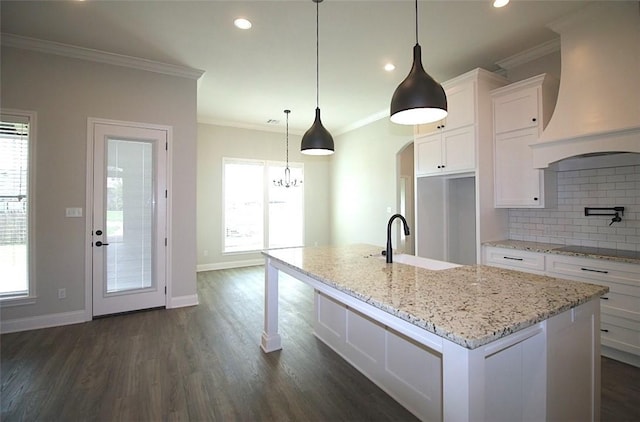 kitchen with custom range hood, dark wood-type flooring, a center island with sink, white cabinets, and hanging light fixtures