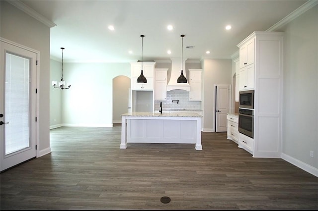 kitchen with appliances with stainless steel finishes, custom range hood, pendant lighting, and a kitchen island with sink