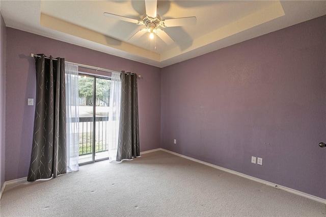 carpeted spare room with a raised ceiling and ceiling fan