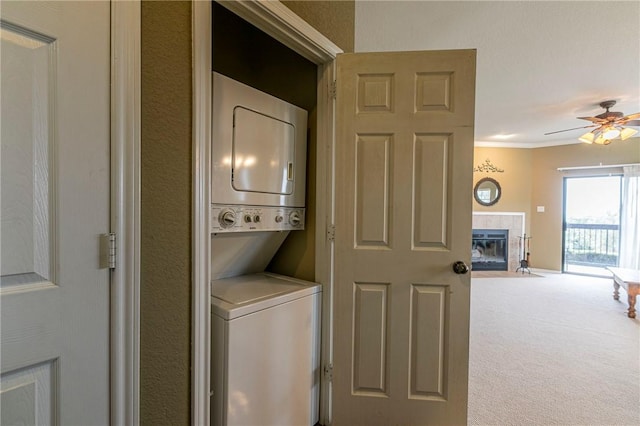 laundry room with a tile fireplace, stacked washing maching and dryer, carpet, and ceiling fan