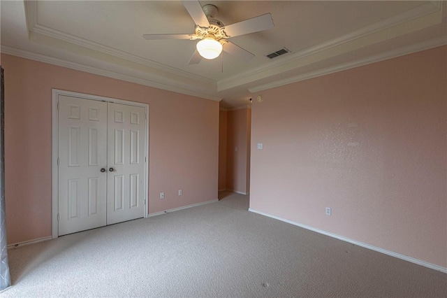 unfurnished bedroom with light carpet, a tray ceiling, ornamental molding, and a closet