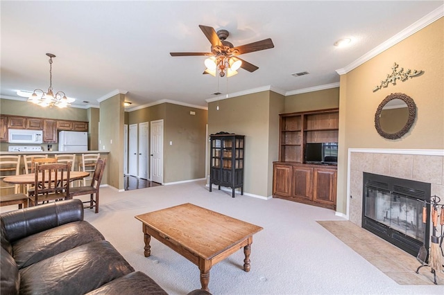 living room featuring light colored carpet, ornamental molding, a tiled fireplace, and ceiling fan with notable chandelier