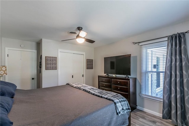 bedroom with light wood-type flooring, two closets, and ceiling fan