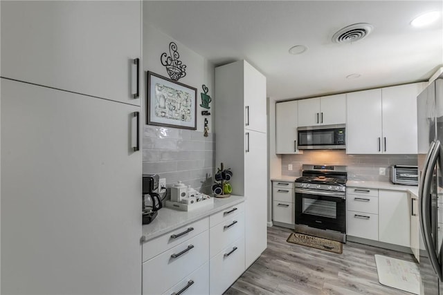 kitchen with decorative backsplash, stainless steel appliances, white cabinetry, and light hardwood / wood-style flooring