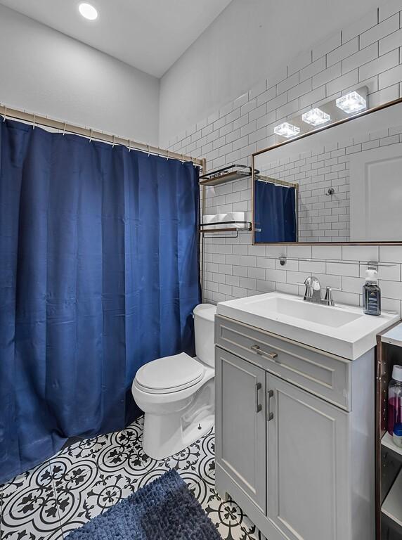 bathroom with tile patterned flooring, vanity, toilet, and tile walls