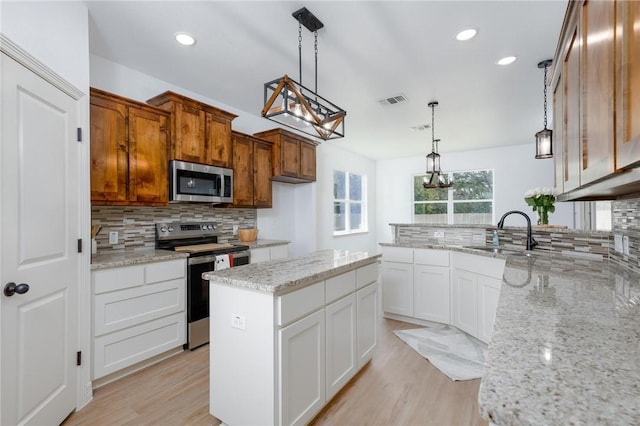 kitchen featuring a center island, light wood-type flooring, decorative light fixtures, white cabinetry, and stainless steel appliances