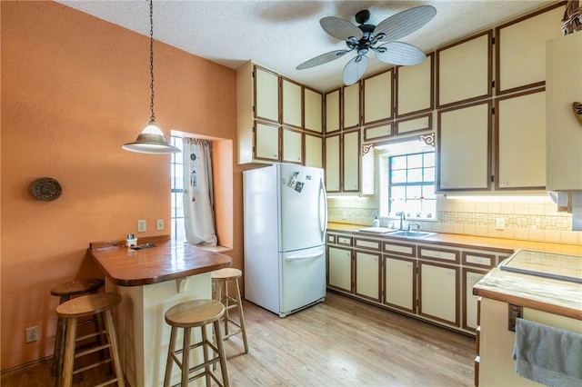 kitchen featuring light wood-style flooring, freestanding refrigerator, pendant lighting, a kitchen bar, and backsplash