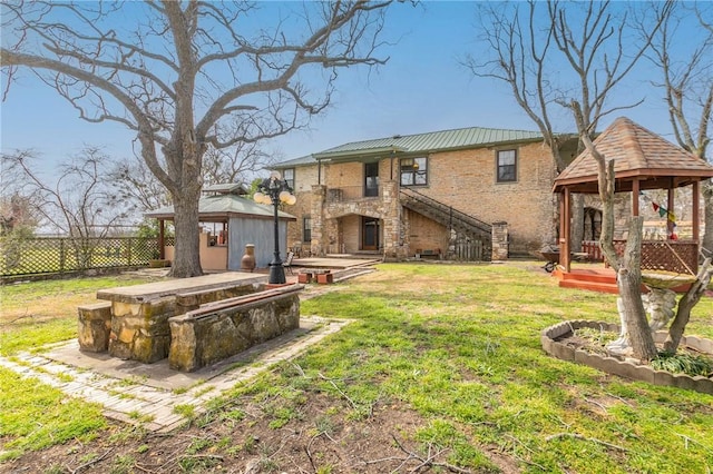 back of house with brick siding, fence, a gazebo, a lawn, and stone siding