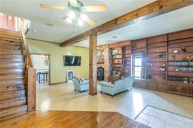 living room with beam ceiling, a wood stove, wood finished floors, and stairway