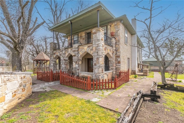 view of front of house with a fenced front yard, stone siding, a chimney, and a balcony