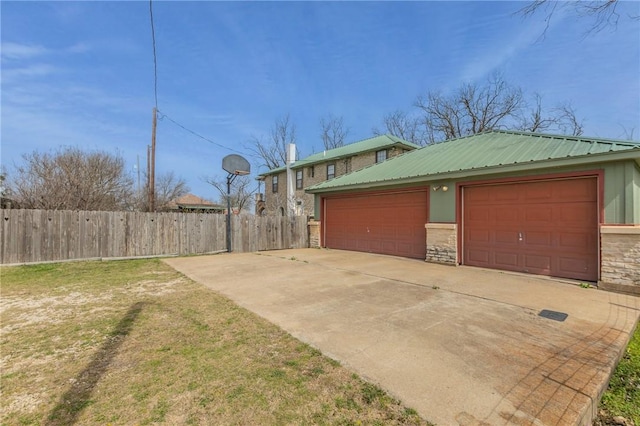 view of home's exterior with a lawn, a garage, stone siding, fence, and metal roof