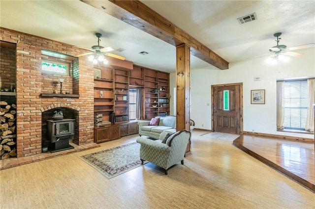 living area with visible vents, ceiling fan, beam ceiling, a wood stove, and wood finished floors