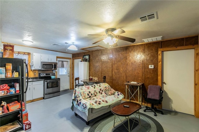 living area featuring visible vents, a textured ceiling, and wooden walls