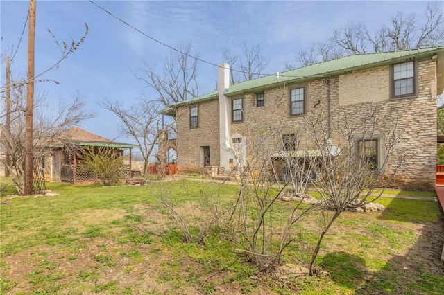 back of property featuring a yard, brick siding, metal roof, and a chimney