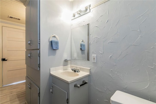 half bathroom featuring visible vents, toilet, vanity, and wood finished floors