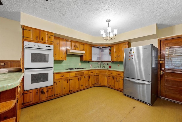 kitchen with backsplash, white appliances, sink, a notable chandelier, and hanging light fixtures