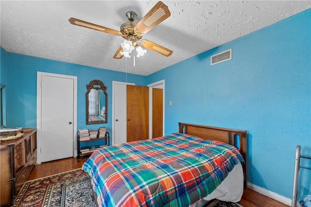 bedroom with a textured ceiling, ceiling fan, and dark hardwood / wood-style floors