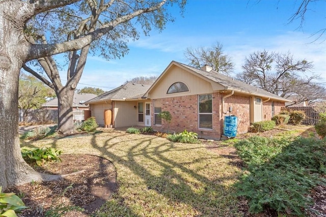 rear view of property featuring brick siding, fence, and a lawn