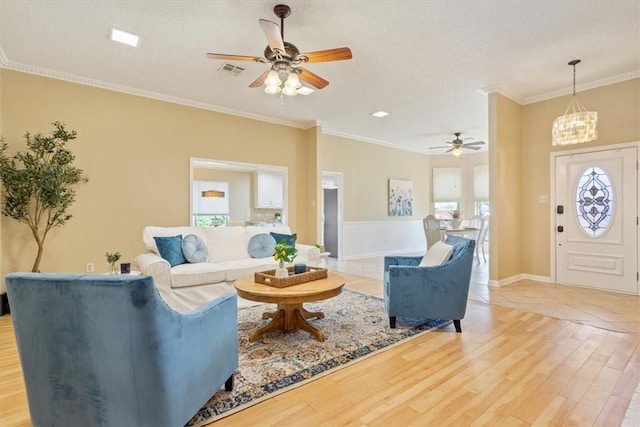 living room with baseboards, visible vents, ornamental molding, light wood-style floors, and ceiling fan with notable chandelier