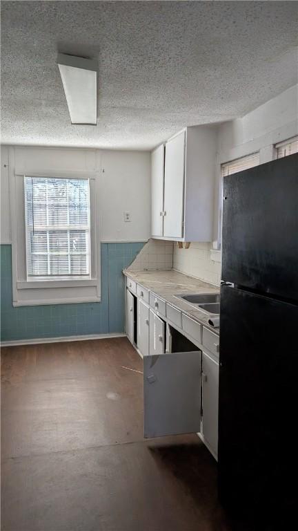 kitchen featuring white cabinetry, black refrigerator, a textured ceiling, and sink