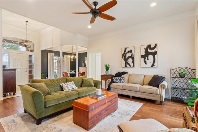 living area with ceiling fan with notable chandelier, ornamental molding, wood finished floors, and recessed lighting