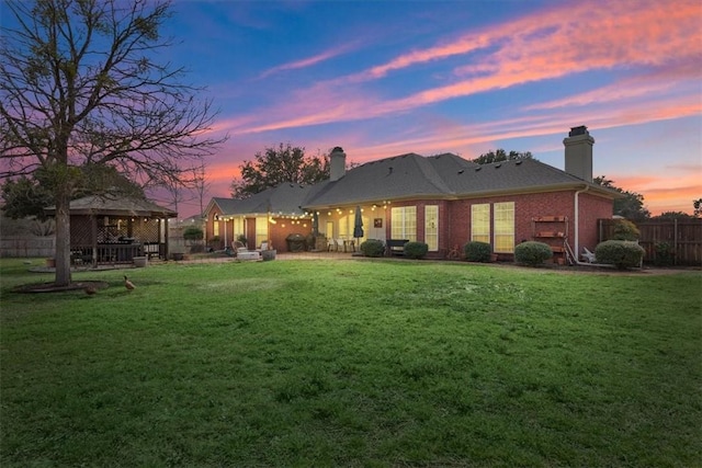 back of house at dusk featuring a yard, a chimney, fence, and a gazebo