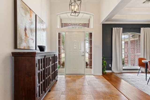 entrance foyer with baseboards, visible vents, crown molding, stone tile flooring, and a notable chandelier