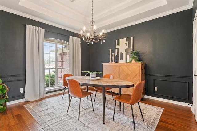 dining space with ornamental molding, a raised ceiling, wood finished floors, and a decorative wall