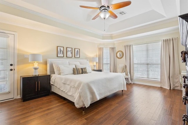 bedroom with ceiling fan, dark wood-style flooring, visible vents, ornamental molding, and a tray ceiling