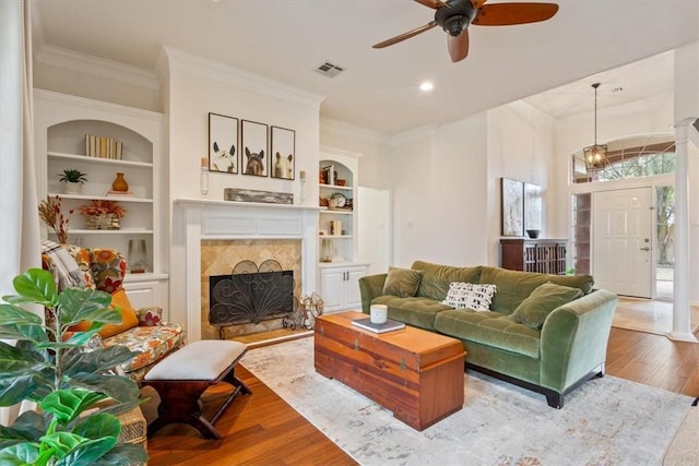 living room with visible vents, crown molding, built in features, and wood finished floors