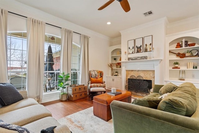 living area with built in shelves, a fireplace, wood finished floors, visible vents, and crown molding