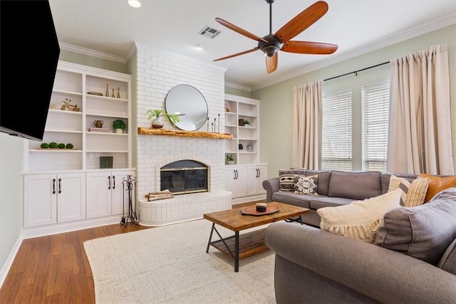 living room with ceiling fan, a fireplace, wood finished floors, visible vents, and crown molding