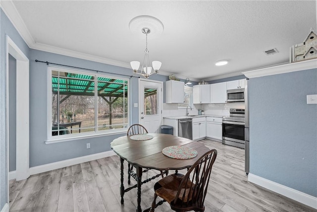 dining space with sink, an inviting chandelier, ornamental molding, and light hardwood / wood-style floors