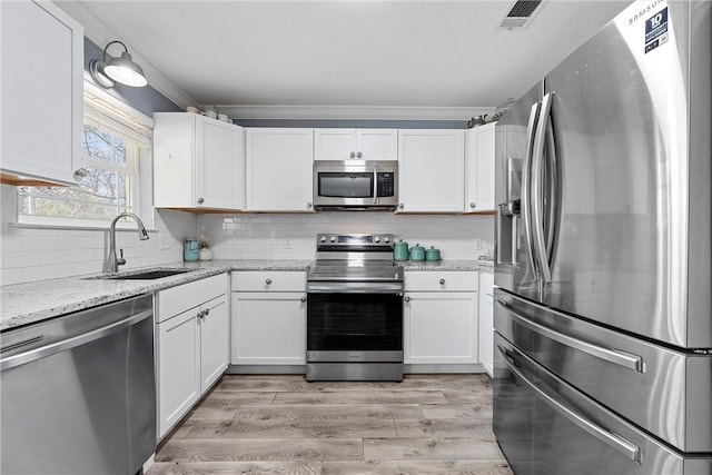 kitchen with light stone countertops, white cabinets, stainless steel appliances, sink, and light hardwood / wood-style flooring