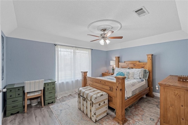 bedroom with ceiling fan, a tray ceiling, a textured ceiling, and light hardwood / wood-style flooring