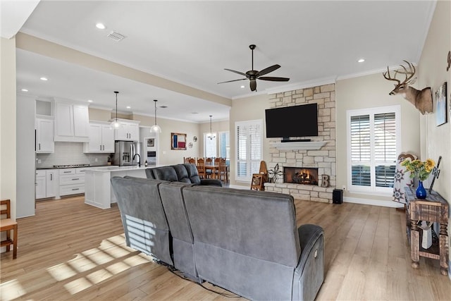 living room featuring a fireplace, light hardwood / wood-style flooring, ceiling fan, and ornamental molding