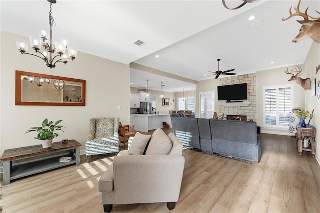 living room with a fireplace, light hardwood / wood-style floors, and ceiling fan with notable chandelier