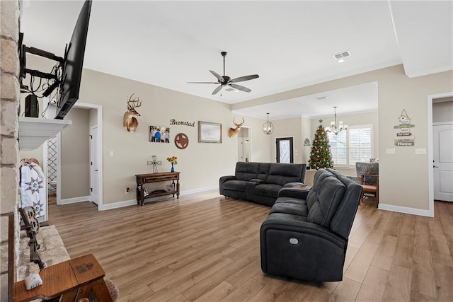 living room featuring ceiling fan with notable chandelier, light hardwood / wood-style floors, a stone fireplace, and ornamental molding