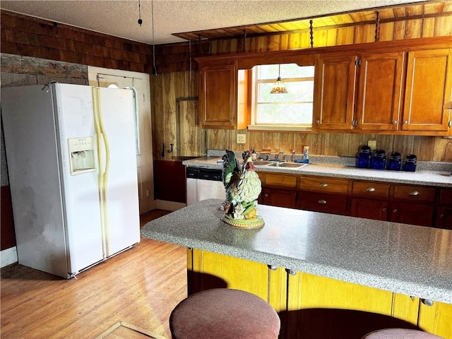 kitchen with sink, stainless steel dishwasher, white refrigerator with ice dispenser, wooden walls, and light wood-type flooring