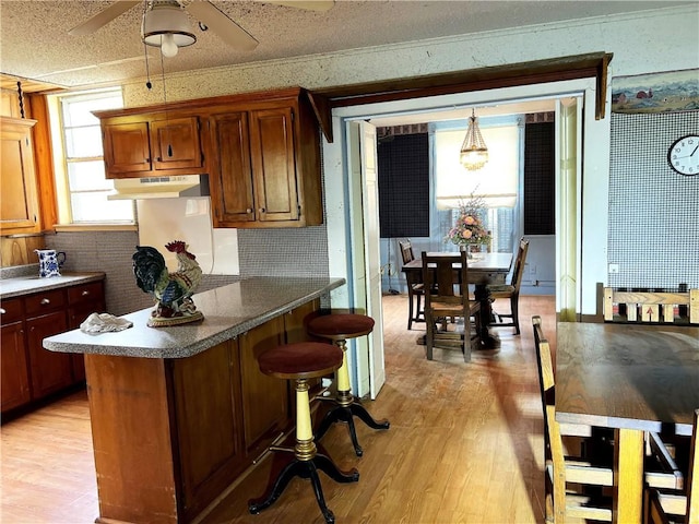 kitchen with a kitchen breakfast bar, light wood-type flooring, a textured ceiling, ceiling fan, and hanging light fixtures