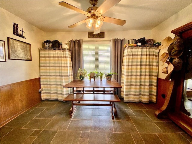 dining space featuring ceiling fan and wood walls