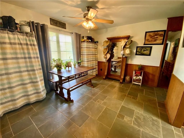 dining space with ceiling fan and wooden walls