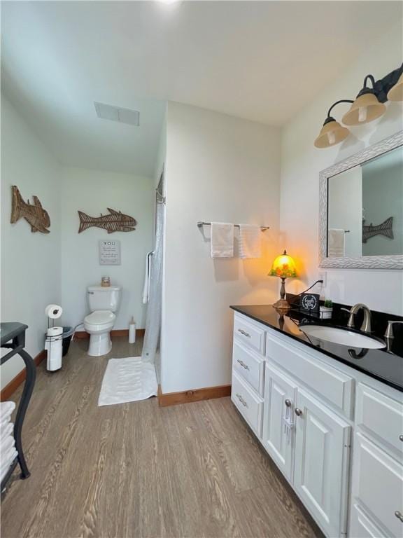 bathroom with wood-type flooring, vanity, toilet, and walk in shower