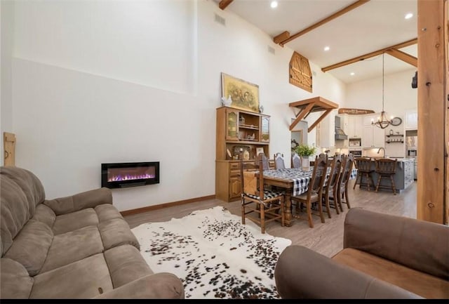 living room with light hardwood / wood-style floors, beam ceiling, high vaulted ceiling, and an inviting chandelier