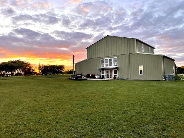 back house at dusk with central air condition unit, a patio area, and a yard