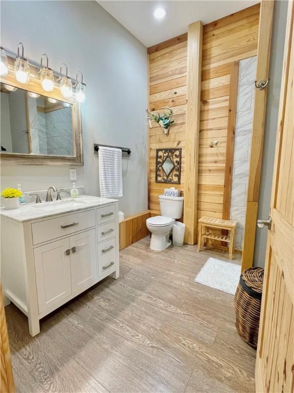 bathroom featuring vanity, hardwood / wood-style flooring, toilet, and wood walls