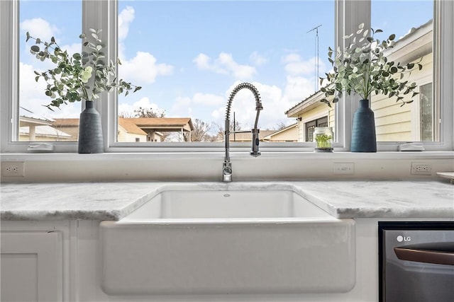 room details with stainless steel dishwasher, white cabinets, light stone counters, and sink