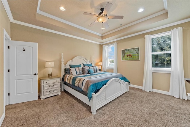 carpeted bedroom featuring ceiling fan, crown molding, multiple windows, and a tray ceiling